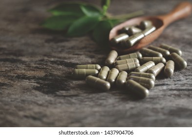 Closed Up Natural Herb Extract In Capsule On Grunge Wooden Background With Some In Spoon Over Blur Green Leaf Background In Dark Tone And Soft Light Filter,selective Focus