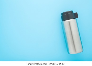 Closed new silver steel thermos with dark black plastic mug for hot drink or soup on light blue table background. Pastel color. Closeup. Empty place for text. Top view. - Powered by Shutterstock