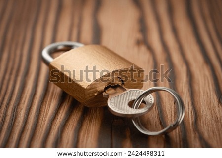A closed padlock with a key inserted into the keyhole. Wooden background. Low angle view.