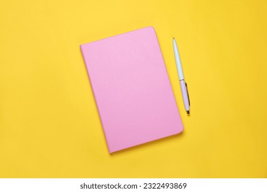 Closed pink notebook and pen on yellow background, flat lay