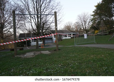 Geschlossener Spielplatz mit Schaukeln aufgrund von Coronavirus.  Eine Metall-Barriere und rot-weiße Barriere-Band-Warnung in deutscher, die Schule ist vorläufig geschlossen, die Nichteinhaltung wird von der Polizei bestraft.
