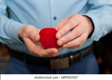 A Closed Red Velvet Ring Box In The Hands Of A Man In A Blue Shirt