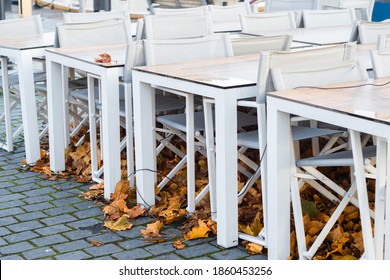 Closed Restaurant, Pub Or Beer Garden Chairs And Tables Folded And Tied During Coronavirus Fourt, Fifth Wave. Old Autumn Leaves Under Empty Gastronomy Seats. Pandemic Problems Of Small Food Business.