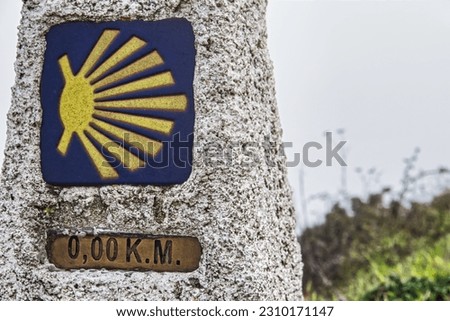 Closed up shoot of the milestone km0 of the Camino de Santiago. Blue background with yellow scallop shell. located in Fisterra, Galicia. Guide for pilgrims. blurred background