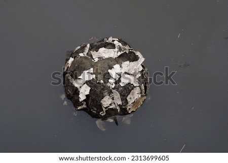 Closed up shot of ragged torn football soccer ball floating on still water concept for damaged environment or sick planet