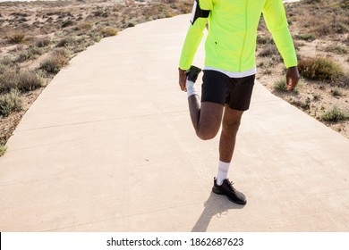 Closed Shot Of A Young Black Runner In A Yellow Rain Jacket Stretching His Legs Before Or After Training.