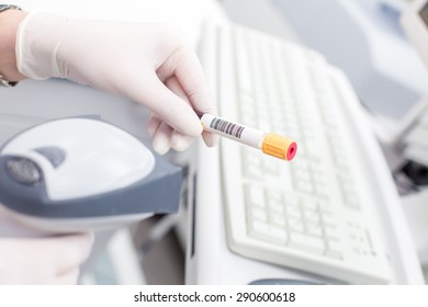 Closed test tube by yellow cap with barcode, read by medical worker in white rubber gloves by  laser scanner for read the bar code in white lab. On background computer keyboard. - Powered by Shutterstock