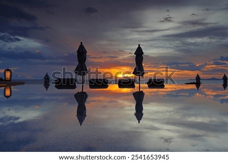 Closed umbrellas reflecting in an infinity pool overlooking the sea in a dramatic sunset sky