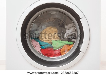 Closed washing machine full of colorful clothes. Closeup. Front view.