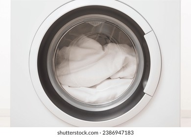 Closed washing machine full of white clothes. Closeup. Front view. - Powered by Shutterstock