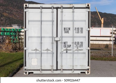 Closed white metal cargo container stands in port area, door face