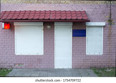 Closed Windows And Office Doors. Facade Of A Store With Door And Shop Windows Closed With White Roll Down Shutters