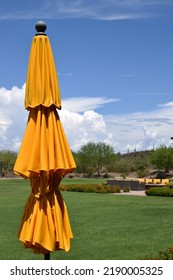 Closed Yellow Umbrella Against Green Grass And Blue Sky