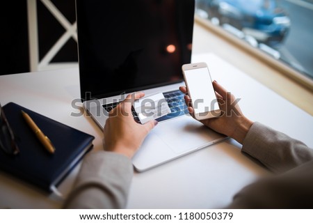 Closely woman business owner makes online purchase via smartphone using debit credit card after work on laptop computer sitting in office interior. Female online shopping store via cell telephone 