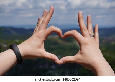 Closer up heart of hands on the naturally blur background of mountains, forests and sky. Love concept.