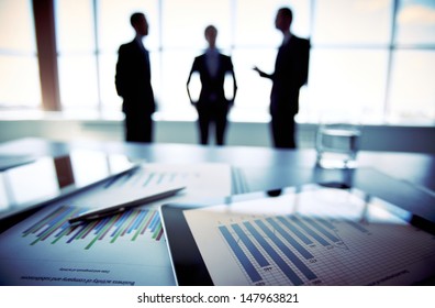 Close-shot of a tablet computer displaying financial data, three businessmen standing in the background - Shutterstock ID 147963821