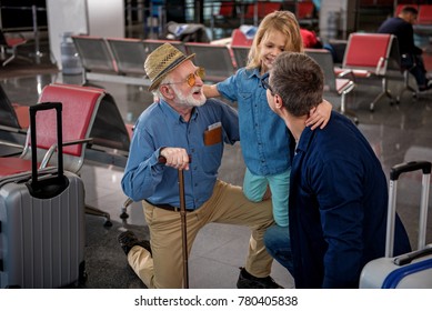 Closest relatives. Top view of cheerful aged man and his adult son are squatting while hugging their little child at airport lounge. They are feeling gladness while looking at each other with joy స్టాక్ ఫోటో