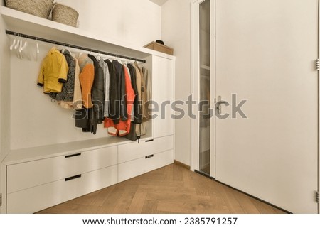 a closet with clothes hanging on the wall and wooden flooring in front of white cabinetd cupboards filled with colorful sweaters