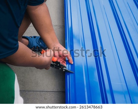 Closeu p of hands using metal snips to cut a blue metal roof sheet. DIY, construction, and home renovation projects