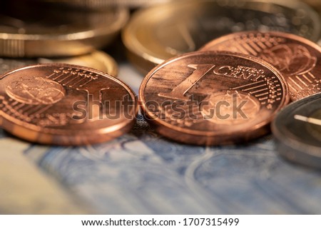 Closeup of 1 Euro cent coin on top of blue 20 euro bill. One Euro coin out of focus in the background. Shortage of money