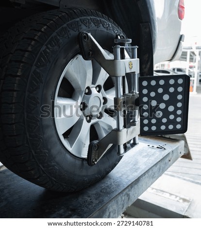 Close-up of 3D wheel alignment target sensor clamped to car alloy wheel for steering and suspension adjustment in auto repair garage, Accuracy Technology Calibration, Car maintenance inspection