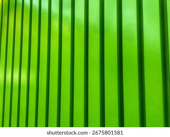 A close-up, abstract image of a surface with vertical green panels or slats. The lighting creates a dynamic pattern of light and shadow, highlighting the texture.