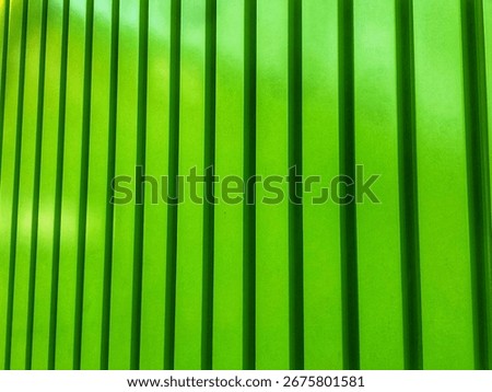 A close-up, abstract image of a surface with vertical green panels or slats. The lighting creates a dynamic pattern of light and shadow, highlighting the texture.