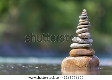 Close-up abstract image of wet rough natural brown uneven different sizes and forms stones balanced like pyramid pile landmark in shallow water on blurred blue-green misty copy space background.