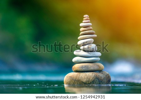 Close-up abstract image of wet rough natural brown uneven different sizes and forms stones balanced like pyramid pile landmark in shallow water on blurred blue-green misty copy space background.