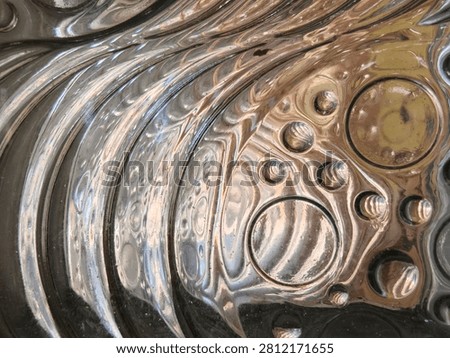 A close-up abstract view of a metallic surface with swirling patterns and circular indentations resembling bubbles.