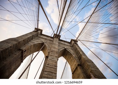 Close-up abstract view of the stone tower arch and steel suspension cables of the Brooklyn Bridge under scenic sunset skies - Powered by Shutterstock