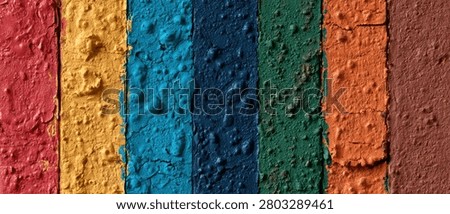 A close-up, abstract view of vertical stripes of paint with a textured, bumpy surface. The colors include red, yellow, blue, dark blue, green, orange, and brown.