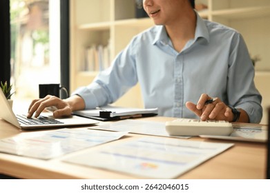 Close-up of an accountant checking financial data with a laptop, calculator, and printed reports on the desk, Auditing Company Financials.