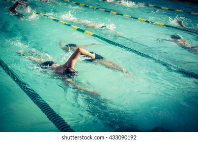 Close-up Action Shot Of Teen Boy Swimming Front Crawl Stroke Style In The Blue Water Outdoor Race Pool. Focus On Arm And Water Splash, Some Motion Blurs. Swimming Race And Competition Concept. Vintage