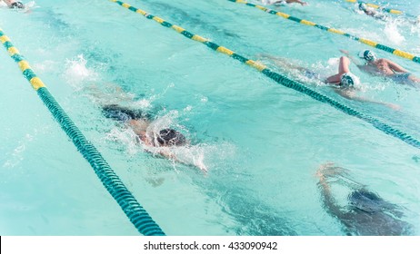 Close-up Action Shot Of Teen Boy Swimming Front Crawl Stroke Style In The Blue Water Outdoor Race Pool. Focus On Arm And Water Splash, Some Motion Blurs. Swimming Race And Competition Concept.Panorama