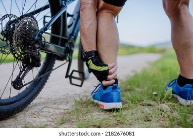 Close-up of active senior man in sportswear suffiering from pain in his ankle after cycling, in park in summer. - Powered by Shutterstock