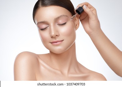 Close-up Adult Woman Beauty Portrait, One Hand Applying Serum On Her Face. Clean Soft Make Up And Isolated White Background.