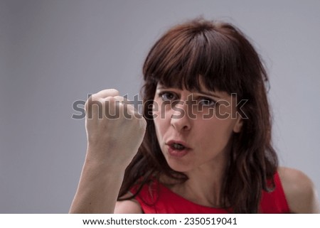 Close-up of an adult woman threatening physical violence, waving a fist near your face. Her expression insults and promises punishment for your faults. Angered, she believes in an eye for an eye