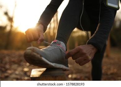 Close-up of African American athlete getting ready for the run and tying her shoelace in the park at sunset. 