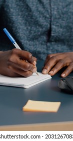 Closeup African American Black Man Hands Taking Notes On Notepad Using A Pen. Male Adult Hands Of Remote Worker Writing Text On White Paper. Business Student In Home Office Handwriting Documents