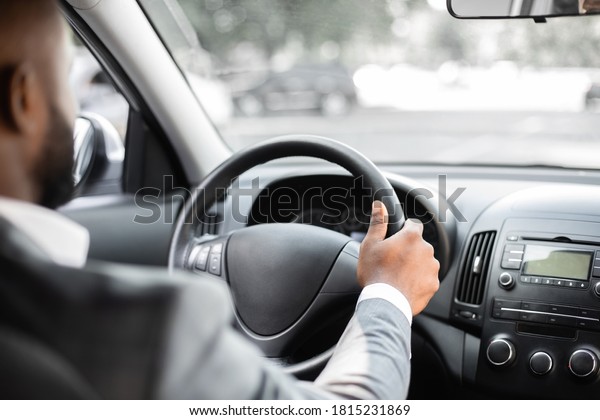 Closeup of african\
american businessman in grey suit driving car, shot from behind.\
Unrecognizable bearded black man driver holding hands on wheel,\
driving luxury car, empty\
space