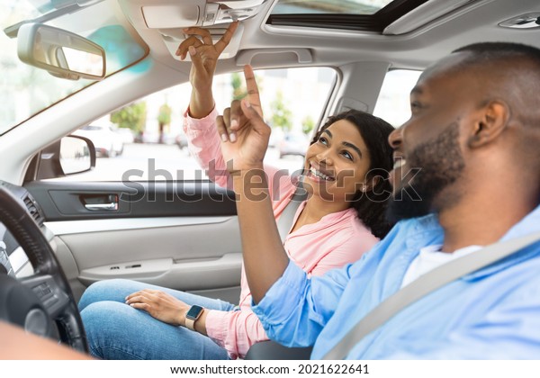 Closeup Of African American Couple Sitting In Car\
Pushing Buttons Opening The Sun Roof On Car Or Examining Vehicle\
Testing Auto In Dealership Showroom. Buying Automobile, Test Drive.\
Selective Focus