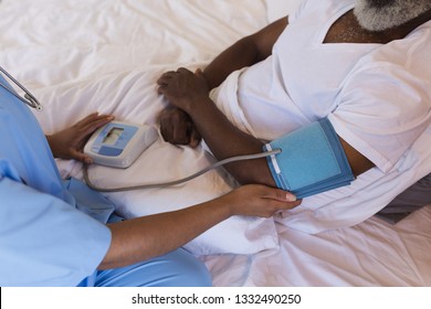 Close-up of African American female doctor measuring blood pressure of senior African American man at home