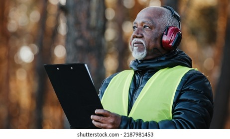 Close-up african american male professional foreman forestry engineer standing outdoors wearing protective headphones assessing situation making tree felling plan writing data reforestation projectt - Powered by Shutterstock