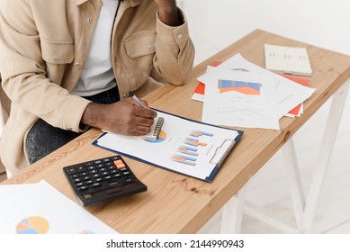 Close-up of an African American man calculating with a calculator, managing household finances, or keeping company financial records at home. Black man making calculations on a calculator, paying - Shutterstock ID 2144990943