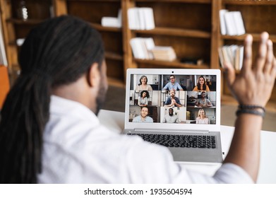 Close-up of African American man with dreadlocks using app for distance video communication with coworkers, friends, meeting online, looking and waving at laptop desktop with people profiles - Powered by Shutterstock