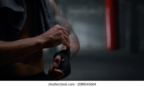 Closeup African American man pulling bandages on hands before boxing training. Athletic guy wrapping hands with punching wraps. Unrecognizable male fighter using boxing tapes for intense workout - Powered by Shutterstock