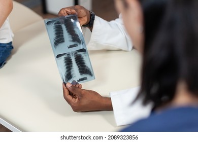 Closeup of african american pediatrician doctor holding lungs radiography in hand discussing medical results during consultation in hospital office. Therapist man analyzing xray. Medicine service - Powered by Shutterstock