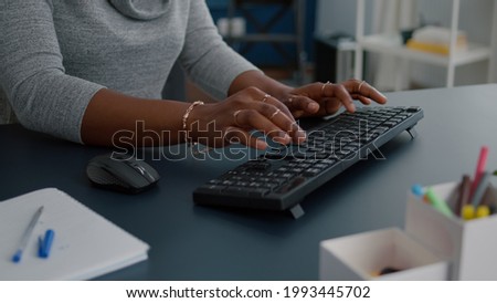 Closeup of african american student hands working at communication project typing information on keyboard using computer sitting at desk in living room. Woman searching business email