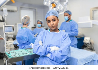 Close-up of a African American surgeon woman looking at camera with colleagues performing in background in operation room. The concept of medicine - Powered by Shutterstock